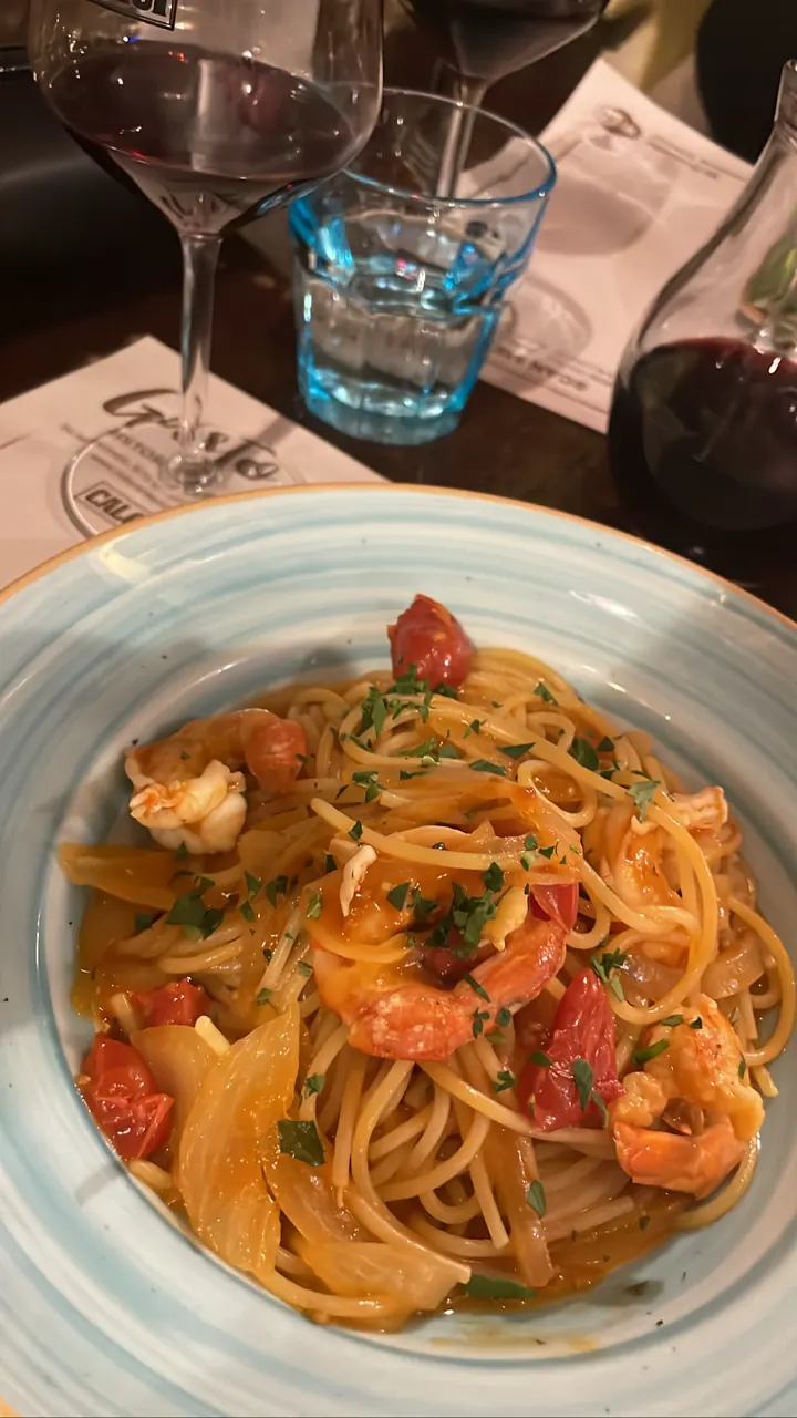 Plate of spaghetti with seafood and tomato beside wine glasses