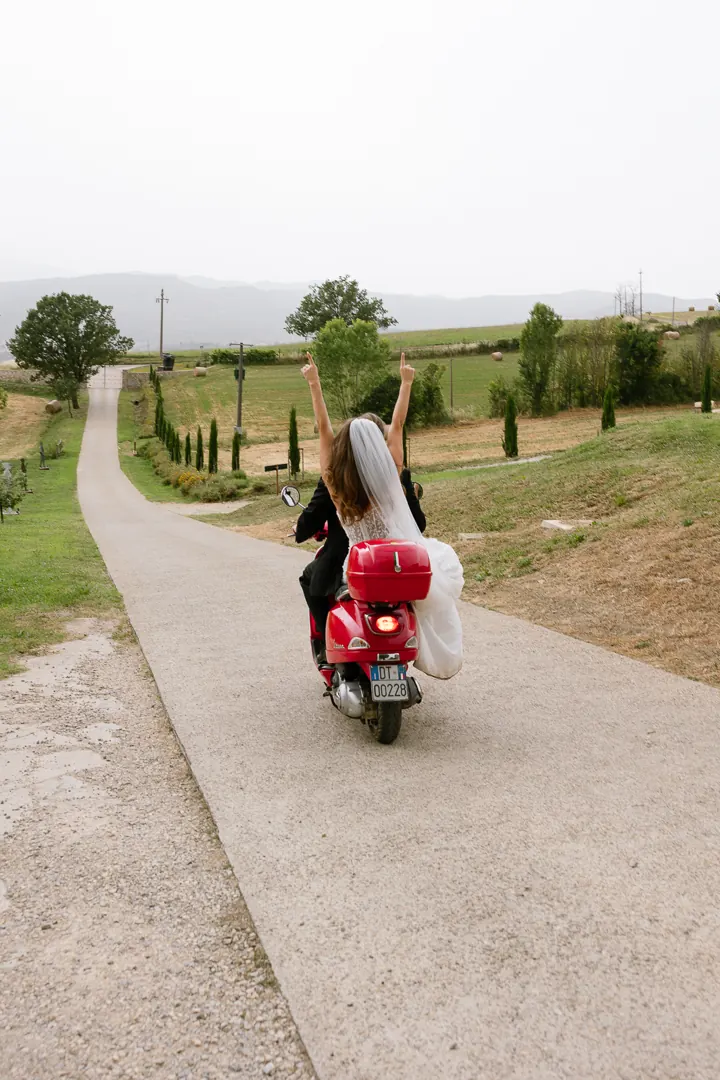 Couple riding a red Vespa along a road through the countryside