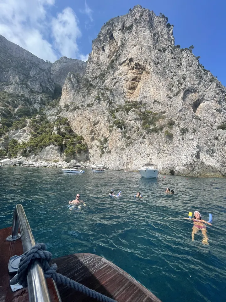 Swimmers in clear water beneath a towering limestone cliff