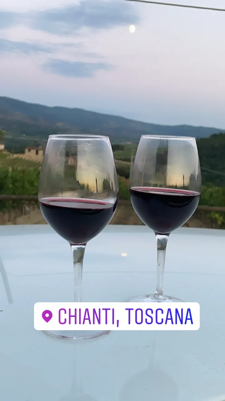 Two glasses of red wine on a table overlooking Tuscan hills
