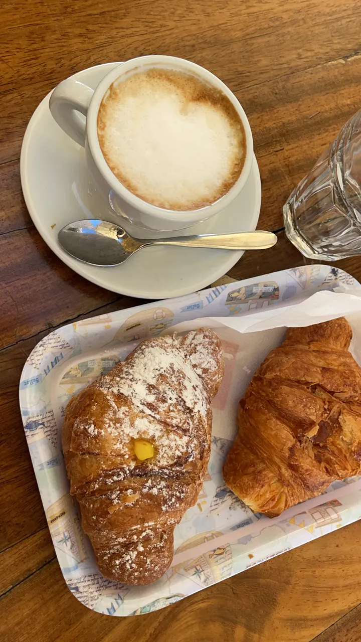 A cappuccino next to a tray of flaky croissants