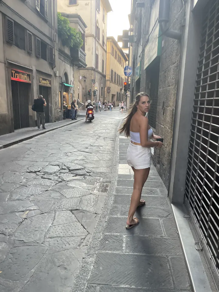 A woman walking down a narrow cobblestone street between stone buildings