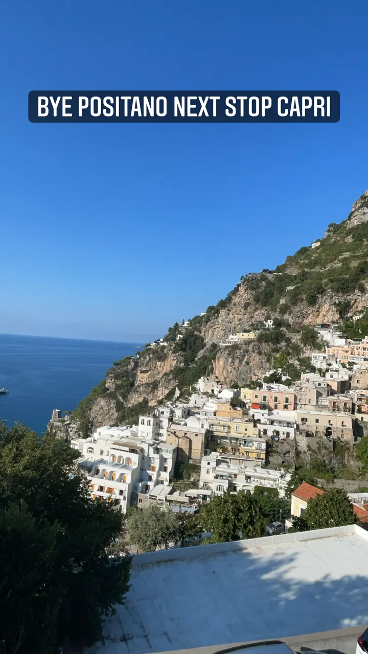 Positano's hillside houses seen from a departing boat, with a 'Bye Positano, next stop Capri' caption