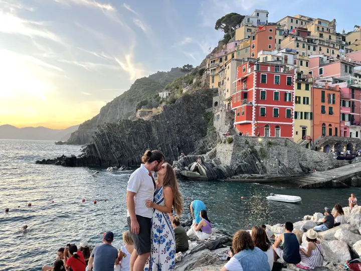 People gathered on the rocks below Riomaggiore's pastel buildings at sunset