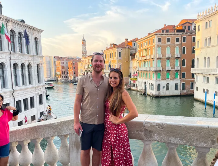 A couple standing on a bridge with colorful buildings along the Grand Canal behind them