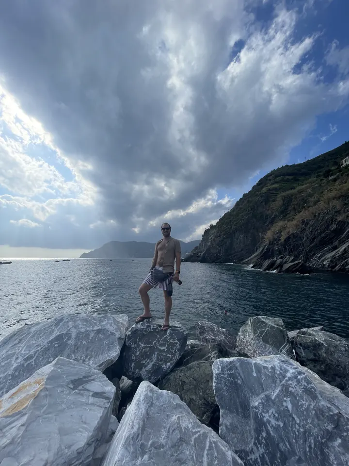 A man standing on breakwater rocks near Vernazza beneath dramatic clouds