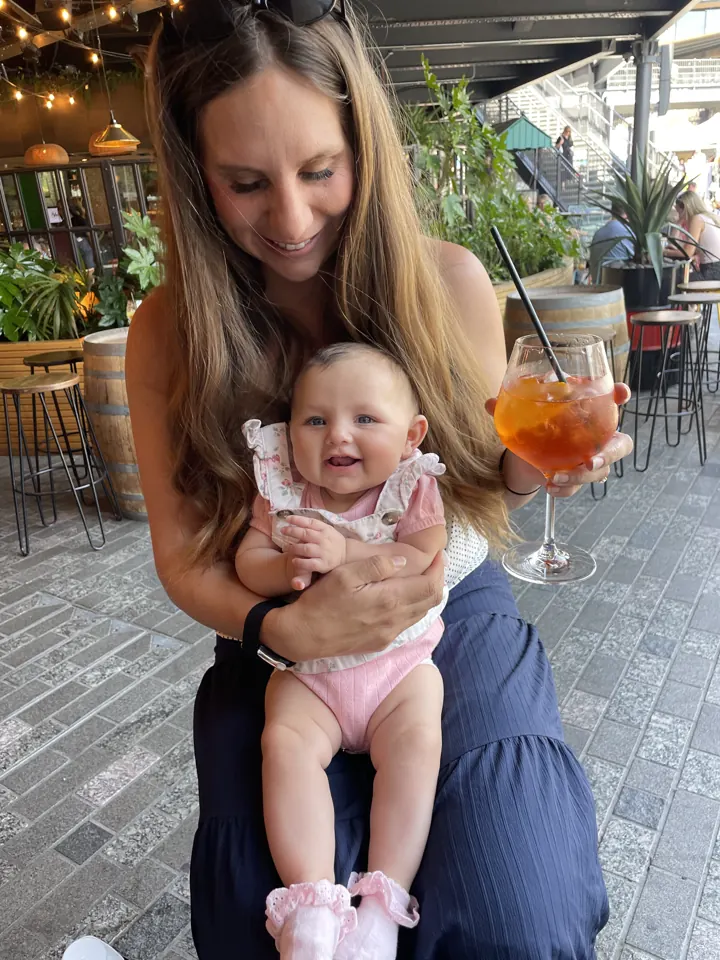 Angela holding a smiling Andi at a café table with a spritz