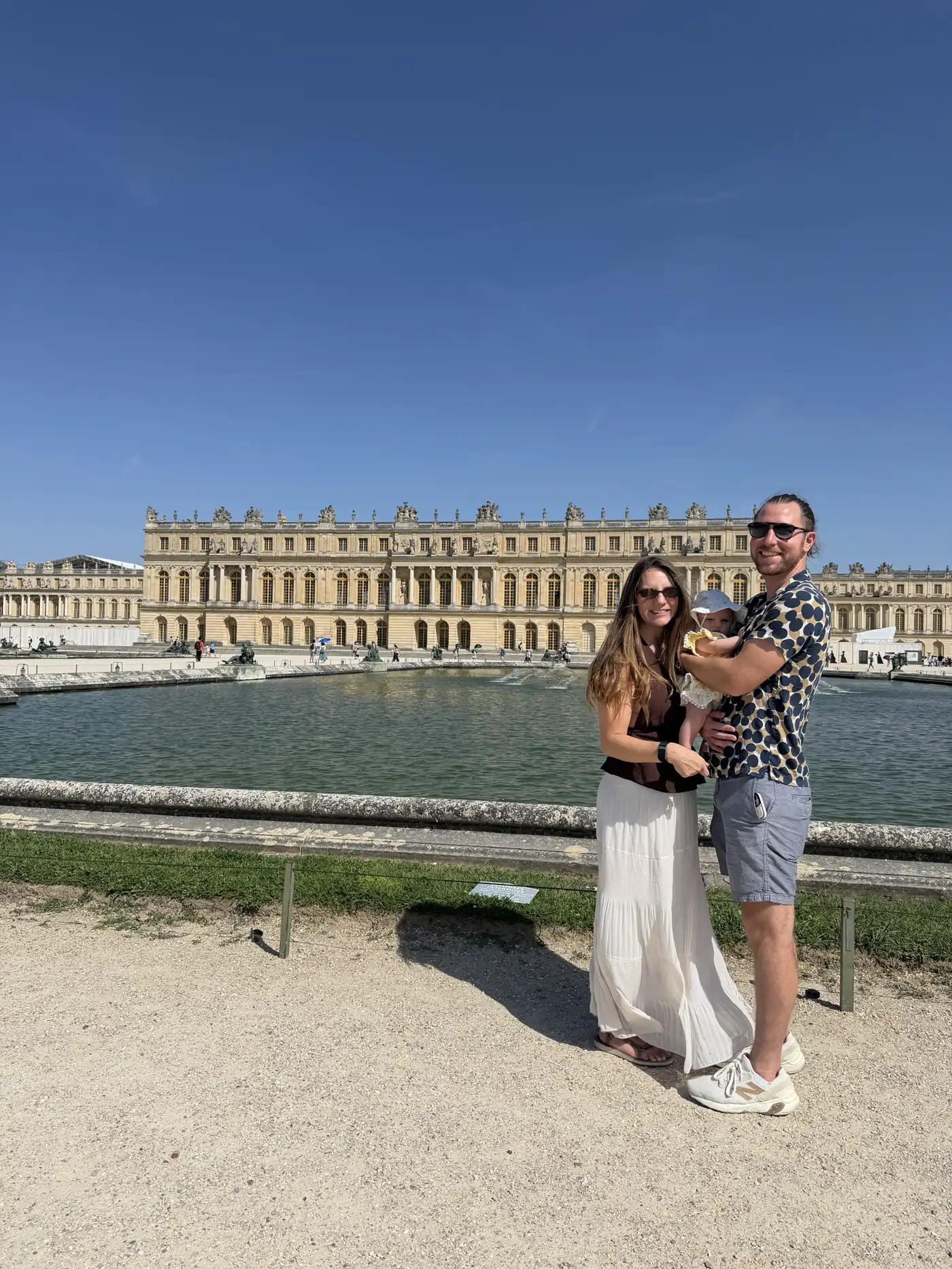 Angela and Colin holding Andi in front of the Palace of Versailles