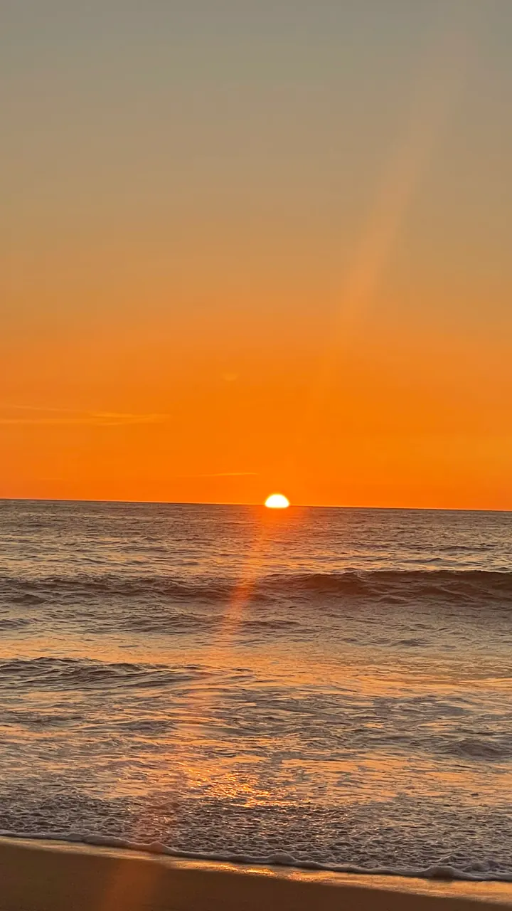 Sun setting into the ocean under an orange sky