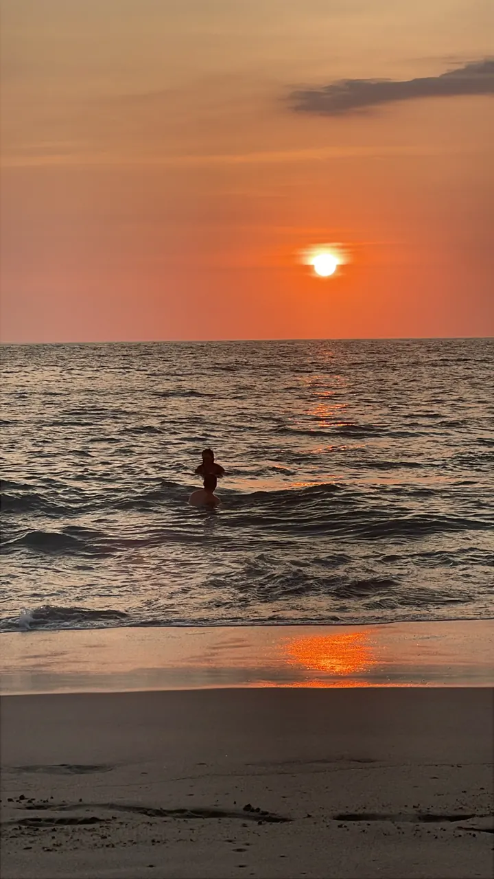 Red sun setting over the ocean with a surfer in the water