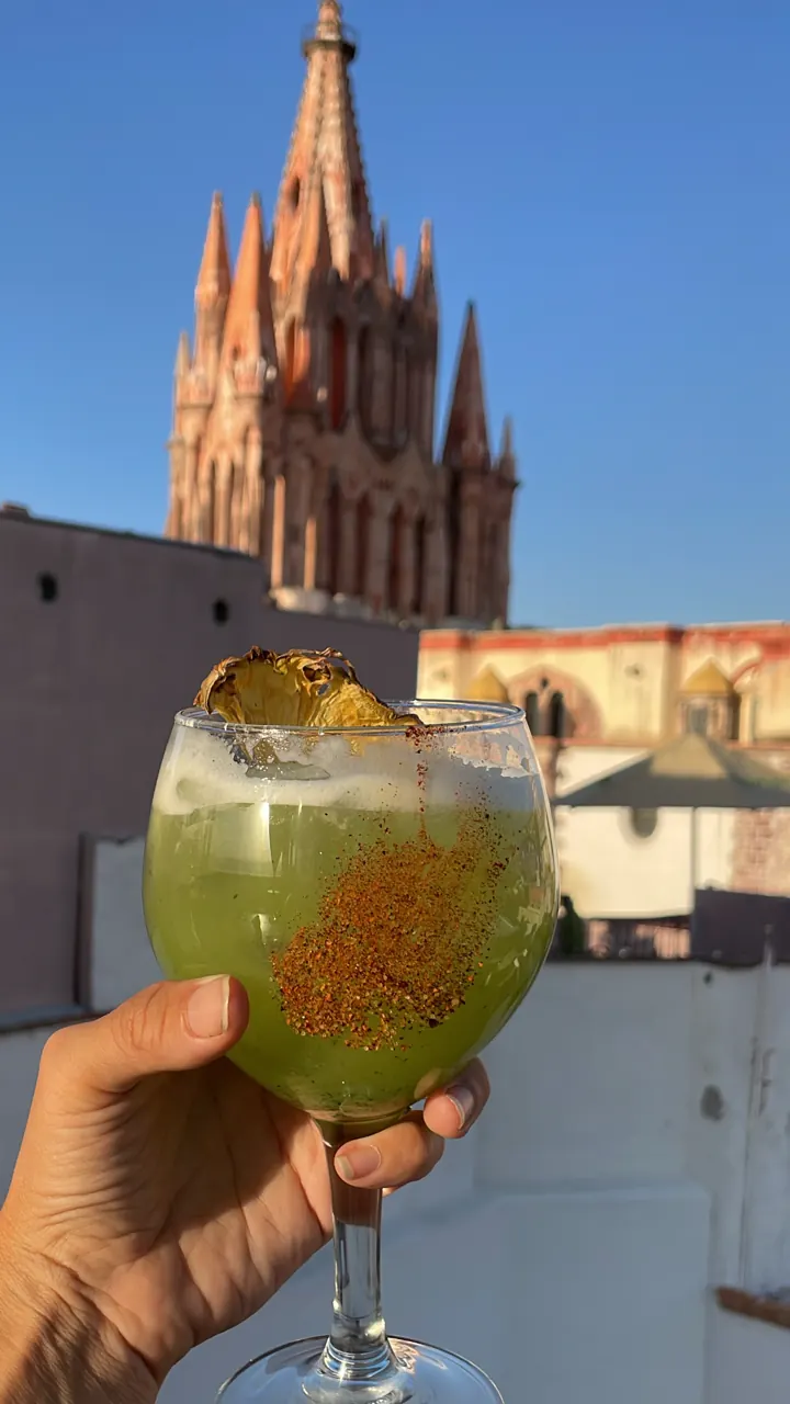 Green cocktail held up in front of the Parroquia's spires