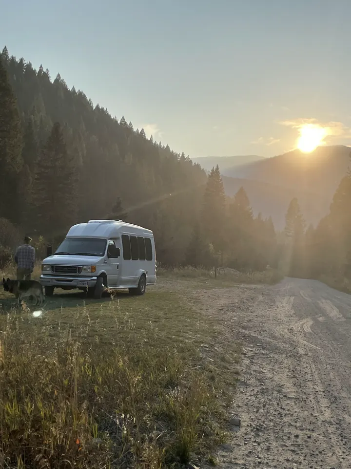 Their white camper van parked in a grassy mountain valley with the sun low over the ridge