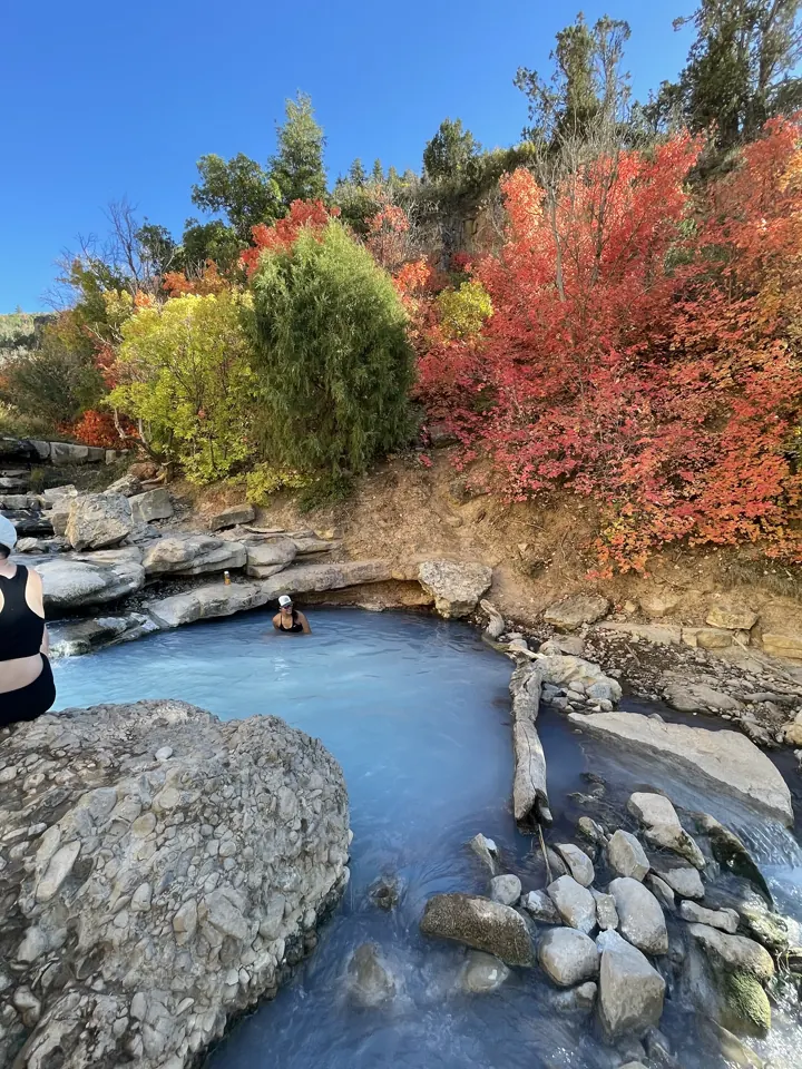 A clear creek pool among rocks, surrounded by red and yellow fall foliage