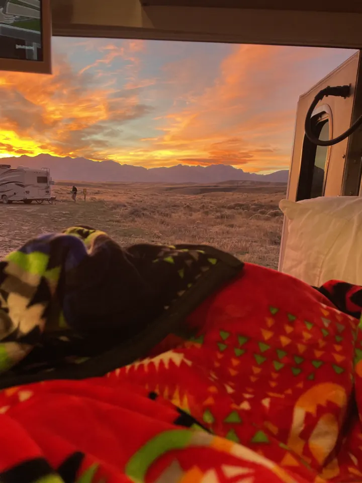 A blazing orange sunset seen from inside the van past a red blanket