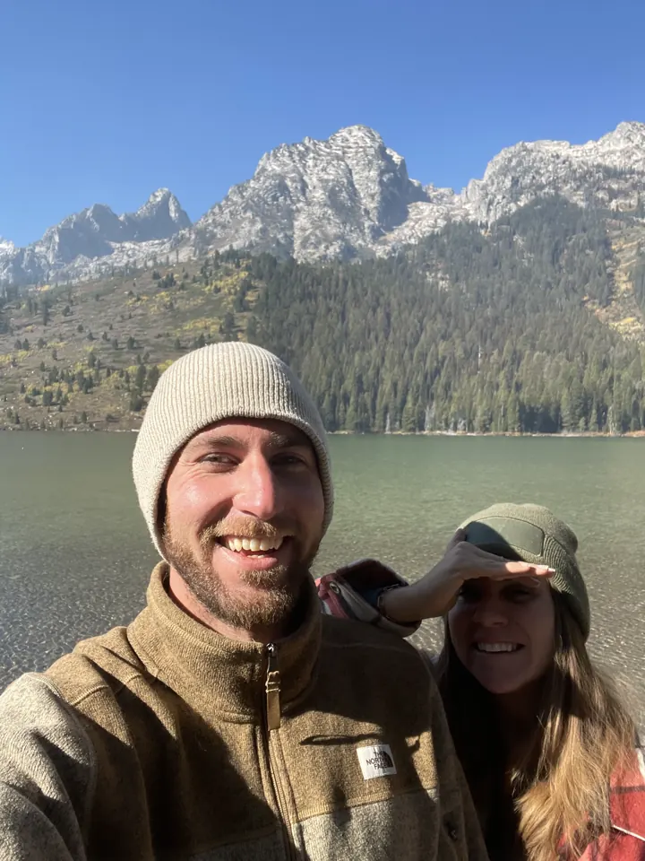 Colin and Angela in beanies taking a selfie in front of a lake and snowy peaks