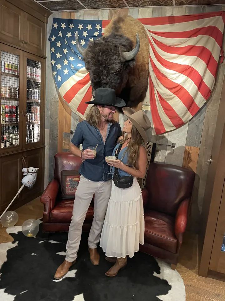 Colin and Angela posing in front of a mounted bison head and an American flag in Park City