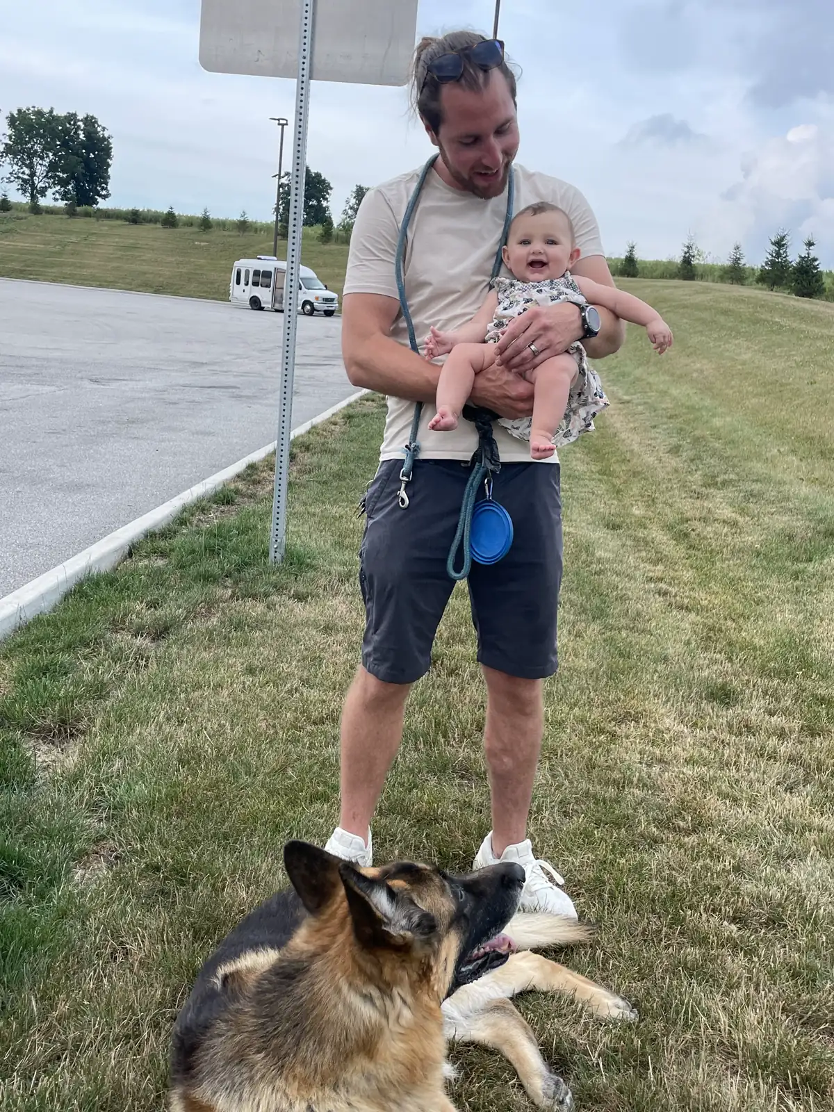 Colin holding Andi at a grassy rest stop while Jack sniffs the ground