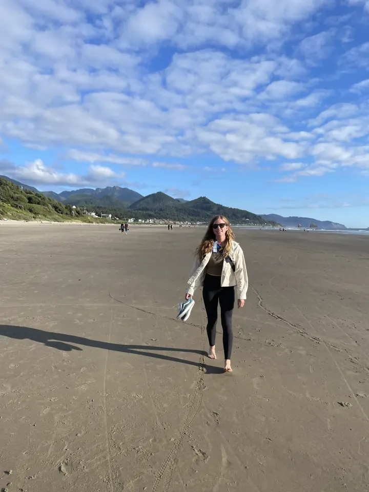 A woman walking on a wide sandy beach under blue sky