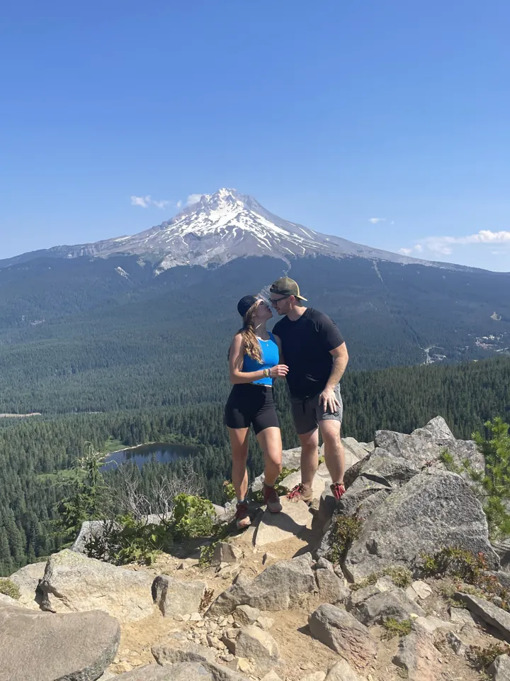 A couple standing on rocks with snowcapped Mount Hood behind