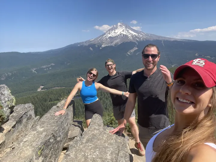 A group of friends on a rocky summit with Mount Hood in the distance