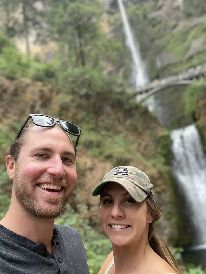 A couple taking a selfie in front of a tall waterfall