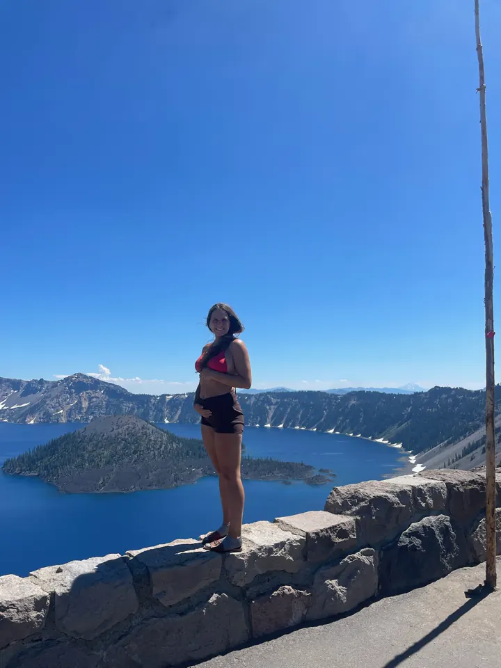 Angela standing on the stone rim wall above Crater Lake and Wizard Island