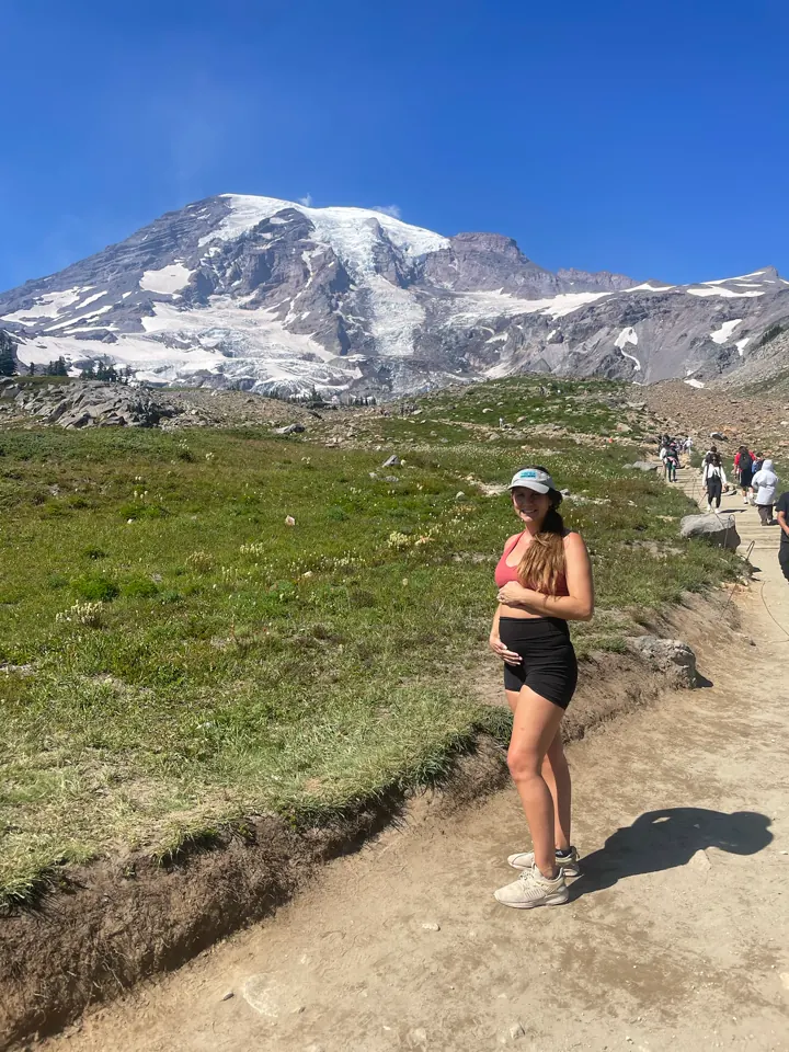 Angela walking a dirt trail with Mount Rainier behind