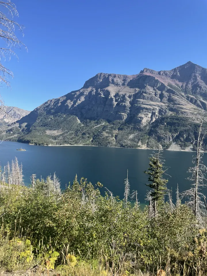 Blue lake below a massive rocky mountain with shrubs in front