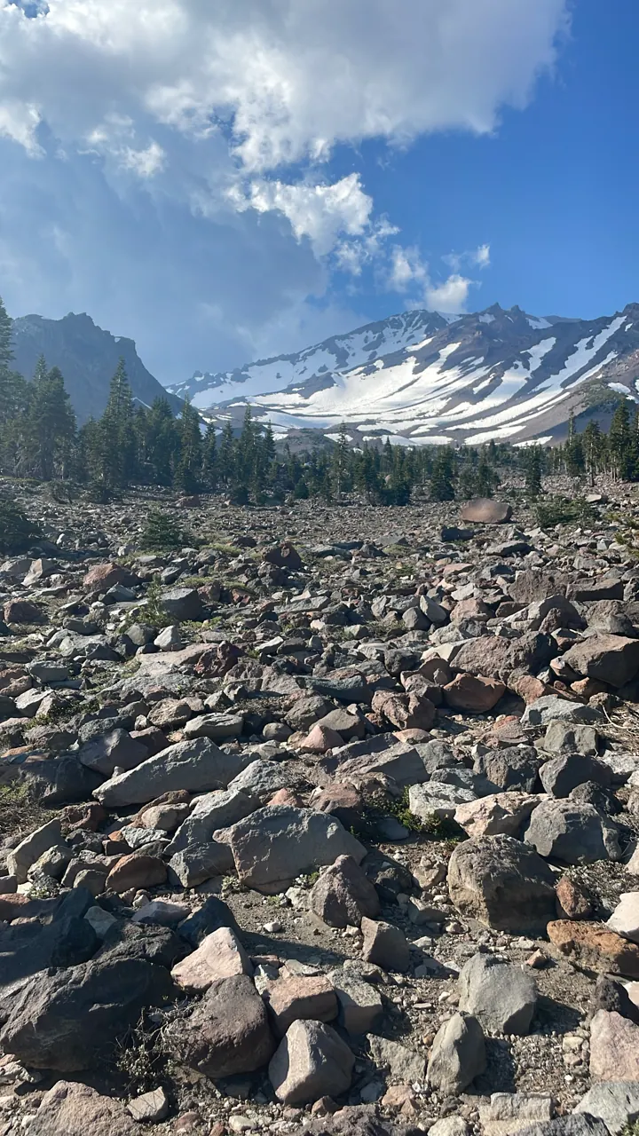Snow-capped Mount Shasta beyond a field of grey rocks under clouds