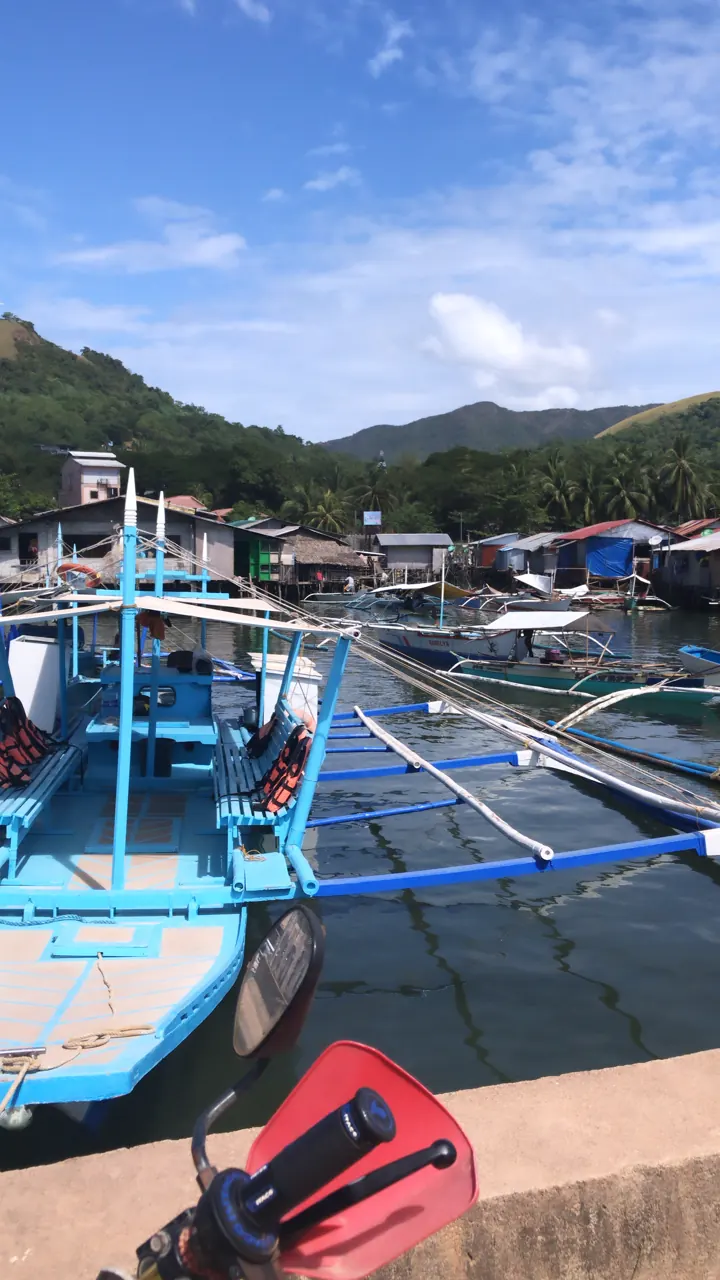 Blue outrigger bangka boats moored at a harbor with stilt houses and green hills