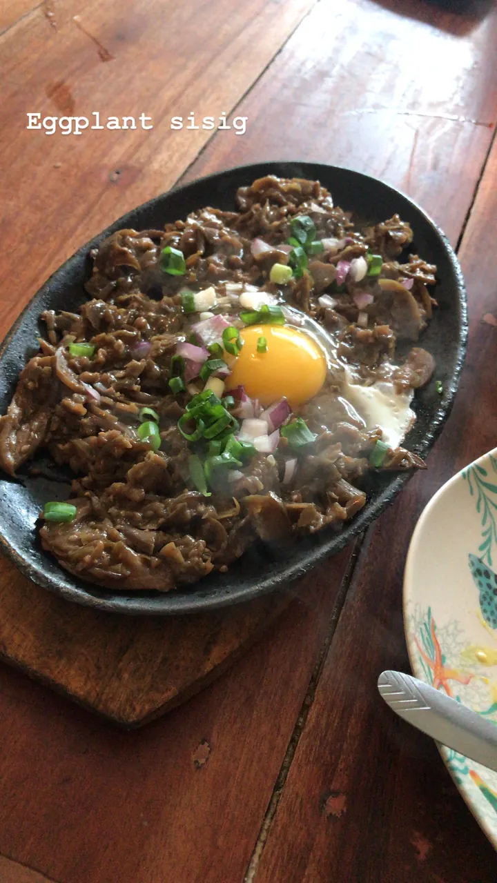 Eggplant sisig on a sizzling plate topped with a raw egg and green onions