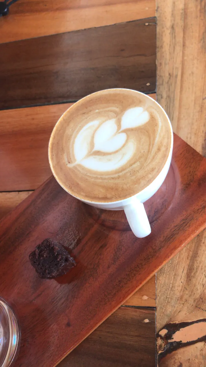 A latte with leaf art in a cup on a wooden board