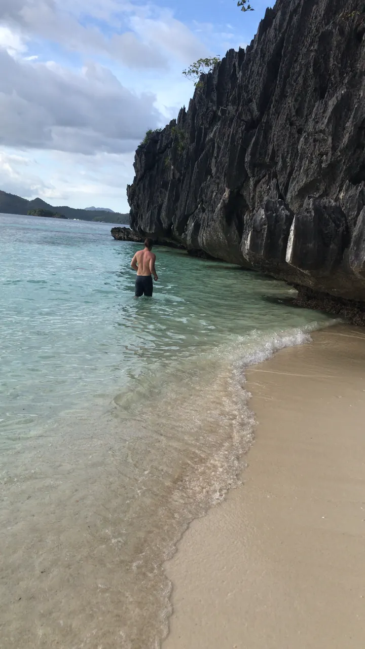 Jagged limestone cliffs above clear shallow water and a white-sand beach in Coron