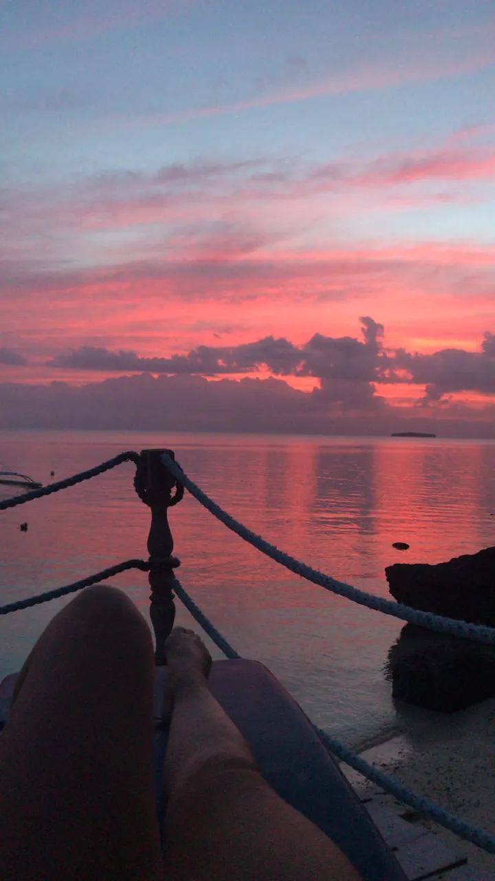 A vivid pink and red sunset seen from the bow of an outrigger boat