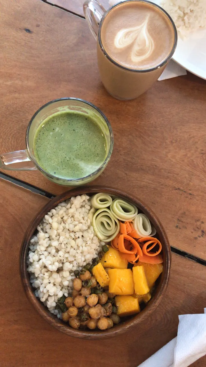 A fruit and granola smoothie bowl with a matcha drink and a latte on a wooden table