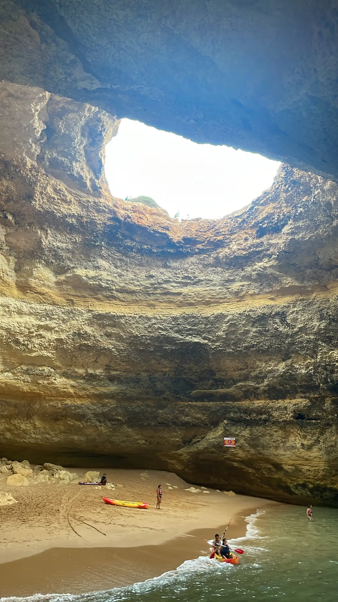 A sea cave with a round opening in the roof above a small beach