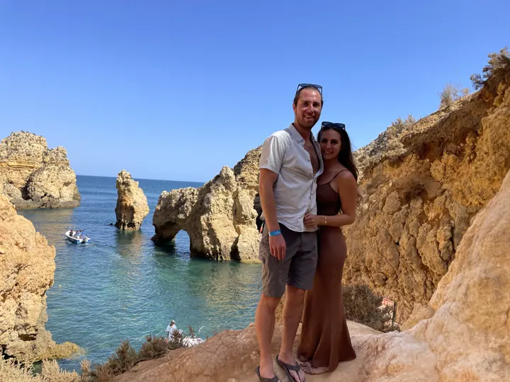 A couple on a clifftop above turquoise water and rock formations