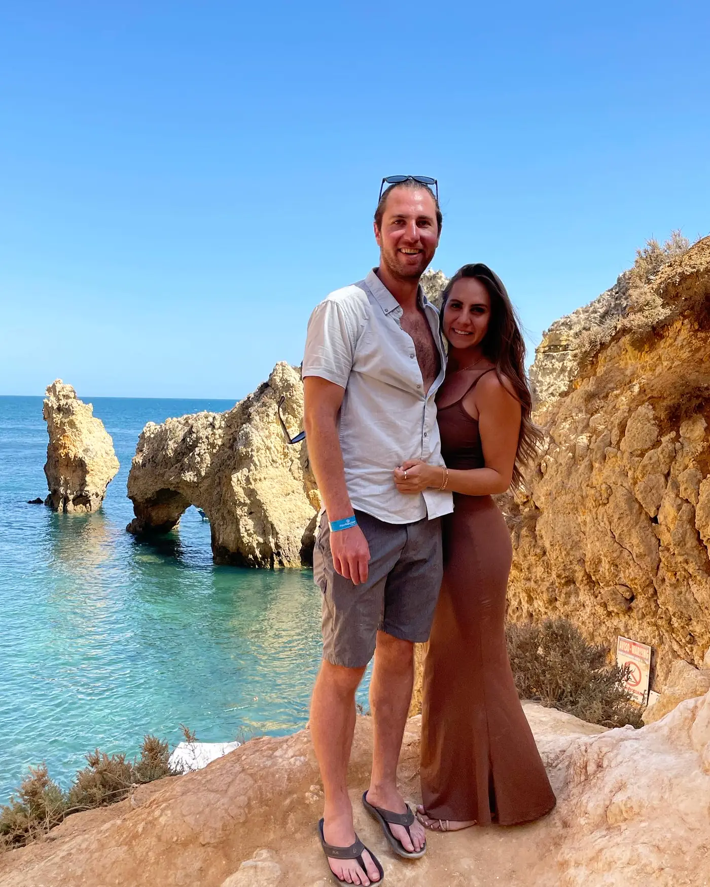 A couple standing on rocky cliffs above turquoise water