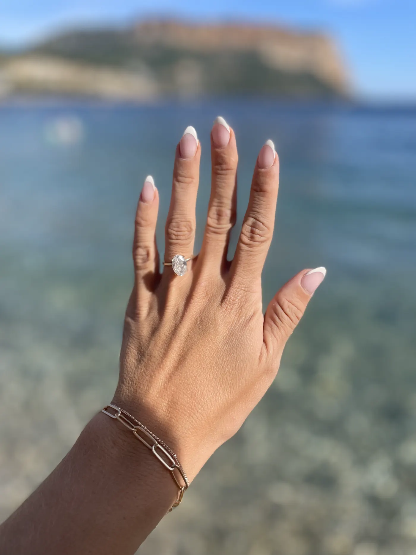 Angela's hand with her new engagement ring, with the sea and cliffs of Cassis behind