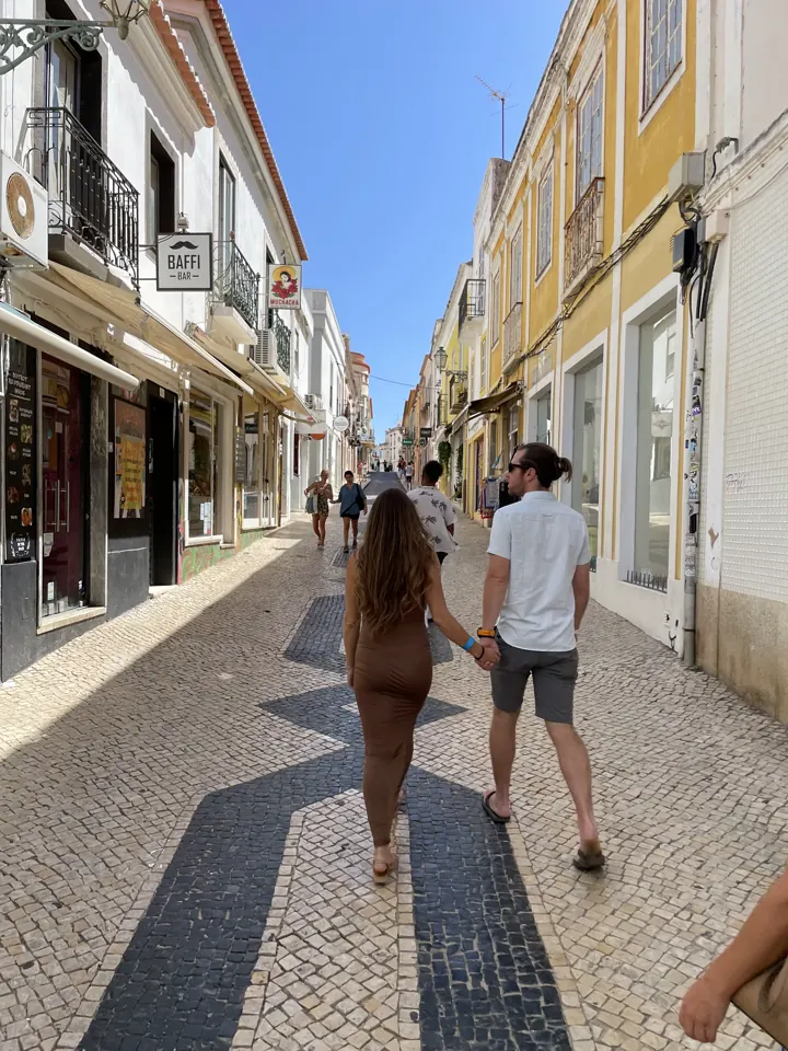 A couple walking down a cobblestone street lined with shops