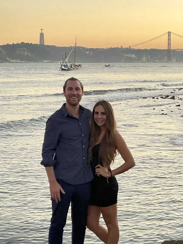 A couple at the waterfront at sunset with a suspension bridge in the distance