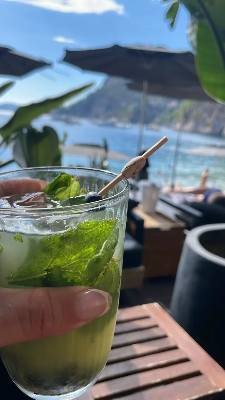 A mojito with mint and lime on a table with the sea behind