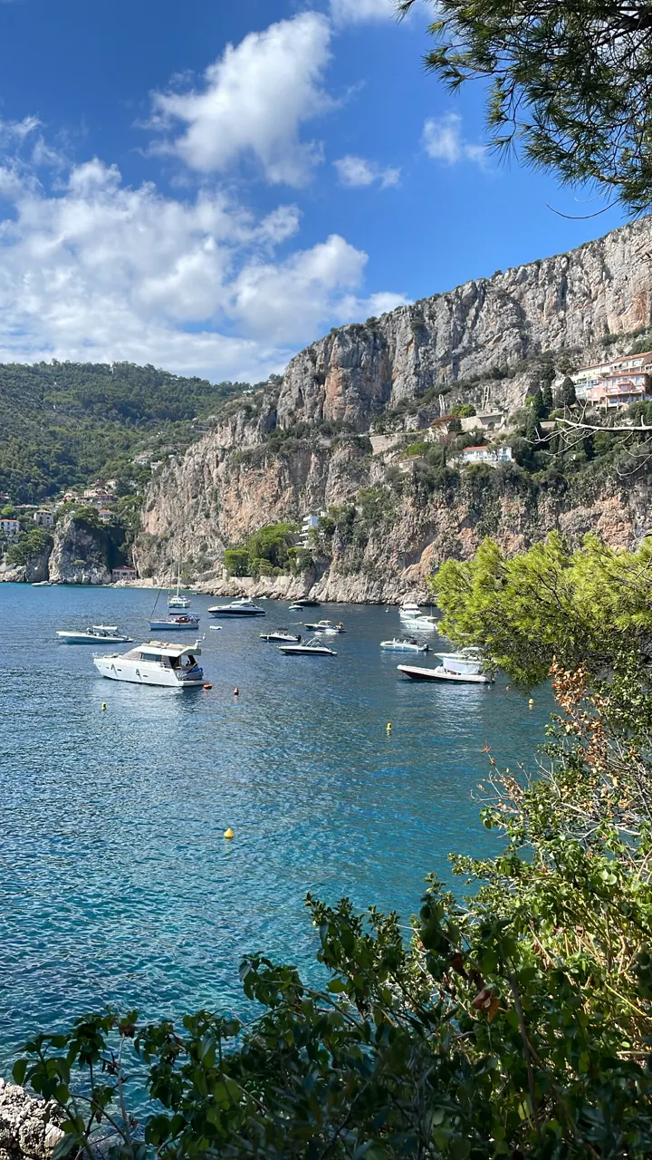 Boats anchored in a blue bay below cliffs and green hills
