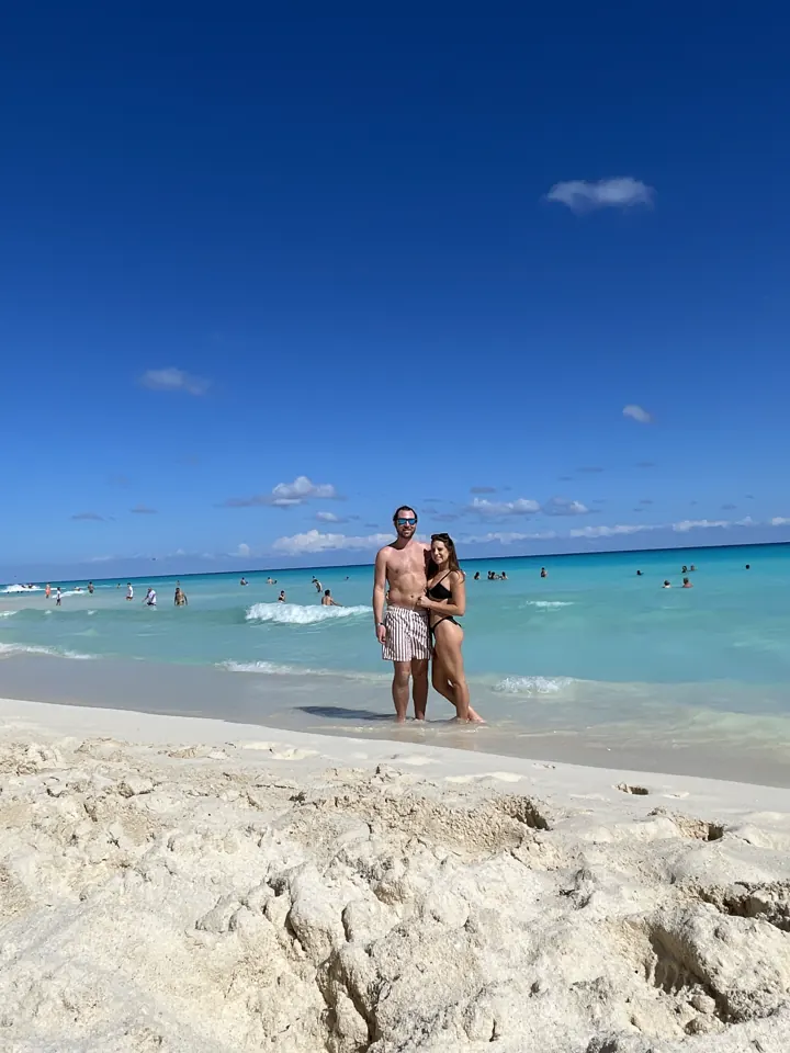 A couple standing on a white-sand beach by turquoise water