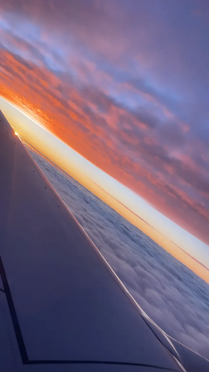 Vivid orange and purple sunset over clouds seen from an airplane window