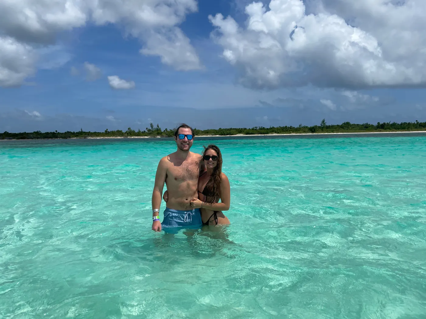 A couple standing waist-deep in clear turquoise water under a blue sky