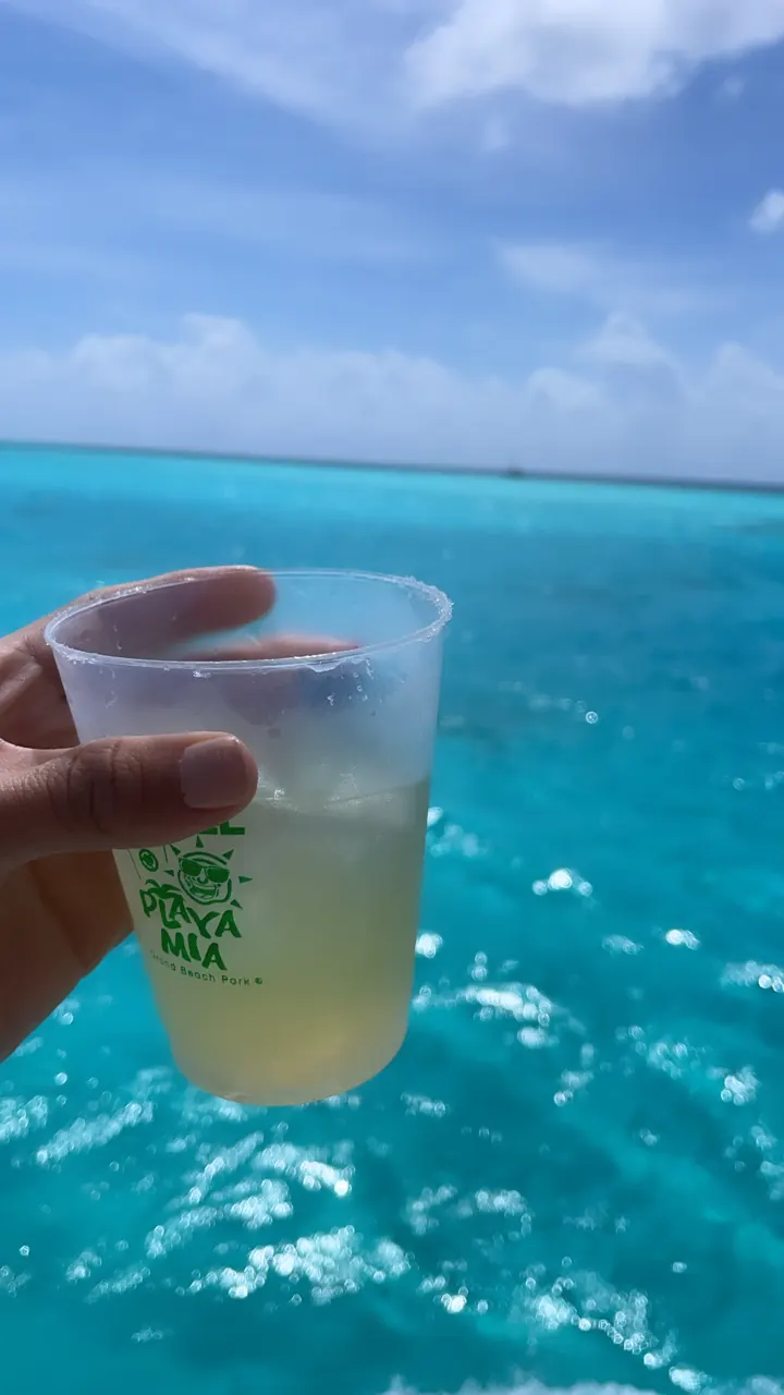 A hand holds a plastic cup of drink over bright blue water