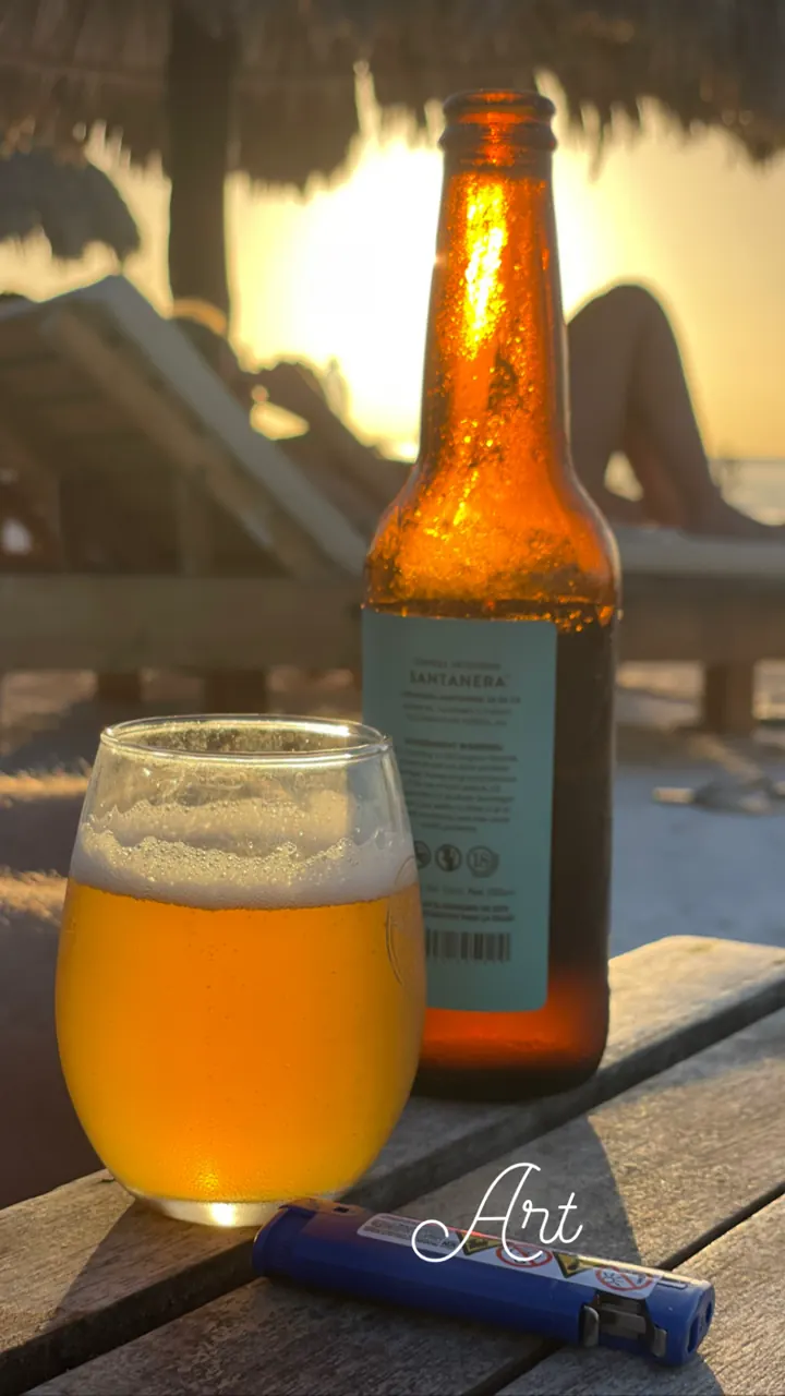 A bottle of beer and a full glass on a table at a beach bar at sunset