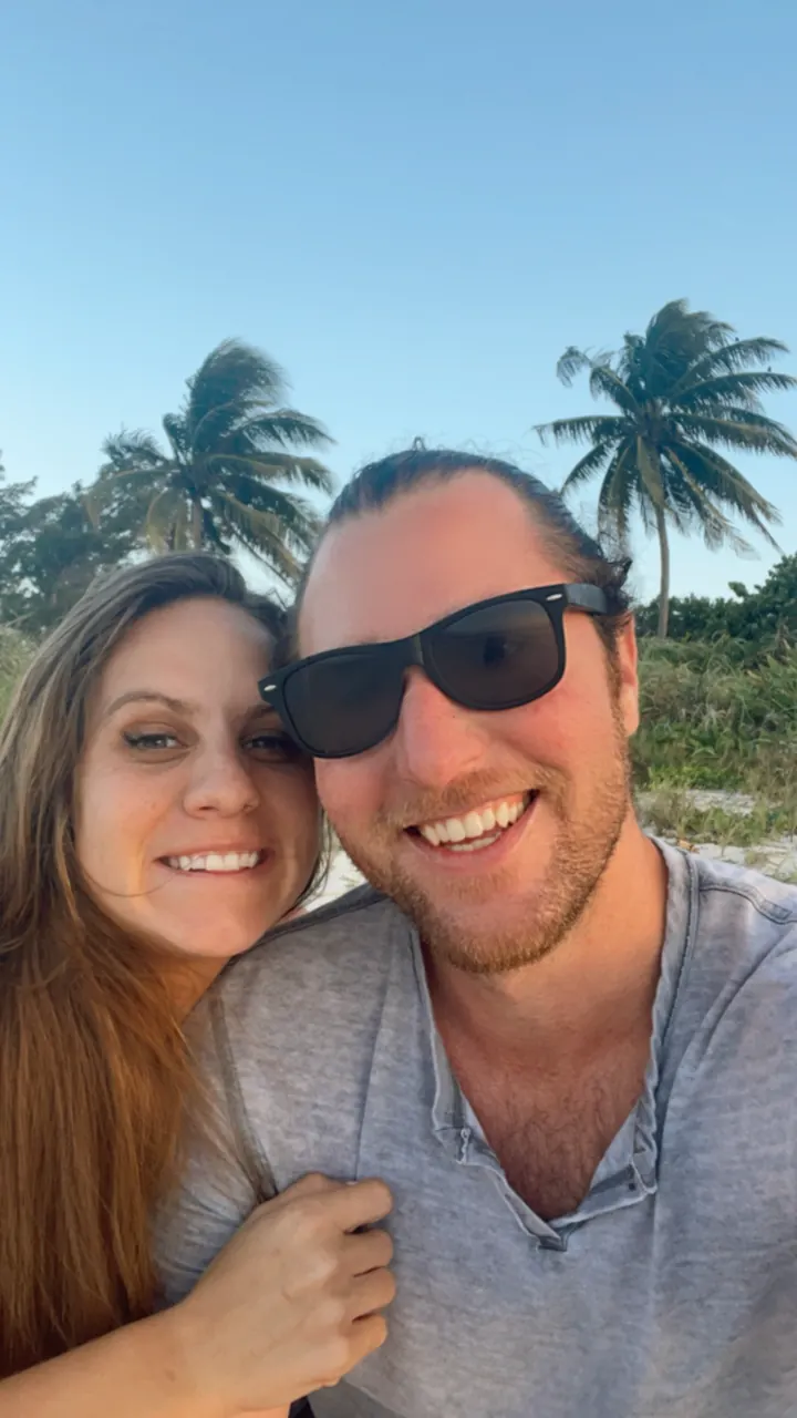 A smiling couple takes a selfie in front of palm trees