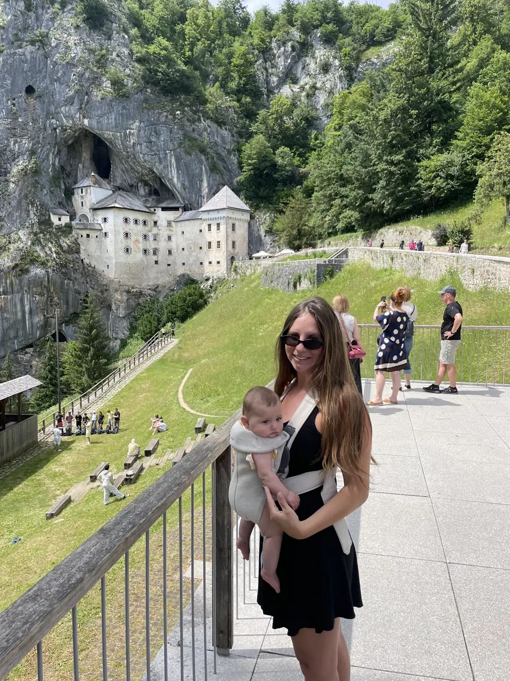 Angela holding Andi in front of Predjama Castle built into a cliff